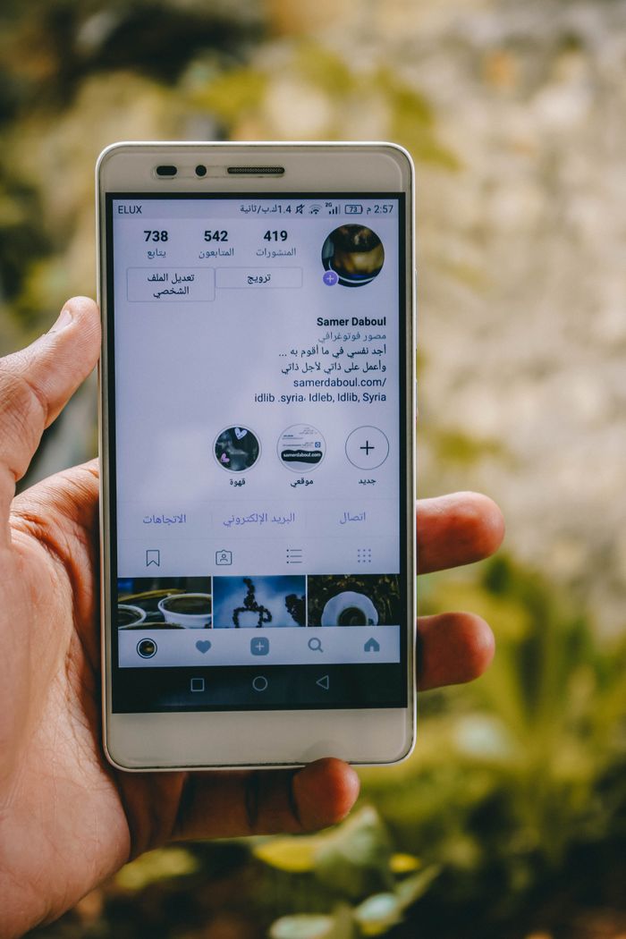 Close-up of a hand holding a smartphone displaying a social media profile outdoors.